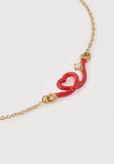 Vörös zománcos szív alakú medál aranyláncon, kis tiszta kő díszítéssel. Egyszerű, ívelt kialakítás sima, fényes felülettel.