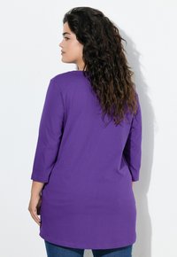 Tunic viola con maniche 3/4, caratterizzata da una vestibilità comoda e una texture morbida. Il capo arriva fino ai fianchi con un orlo arrotondato.