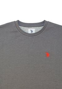 Sweat-shirt gris à col rond avec petit logo rouge brodé d’un joueur de polo sur la poitrine gauche et étiquette intérieure affichant le même logo.