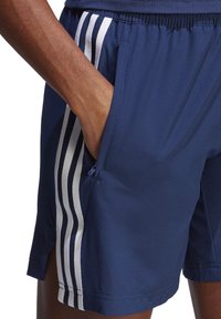 Marineblauwe shorts van lichtgewicht stof met witte zijkanten, voorzien van een elastische tailleband en een zijzak met ritssluiting.