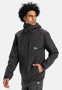 Black waterproof jacket featuring a hood, front zipper, and chest pocket. Notable logo on the left side and adjustable cuffs.