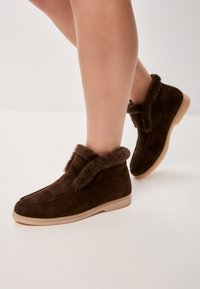 Bottines en daim marron avec un intérieur en fourrure douce, un bout rond et une semelle en caoutchouc clair avec des accents de couture.