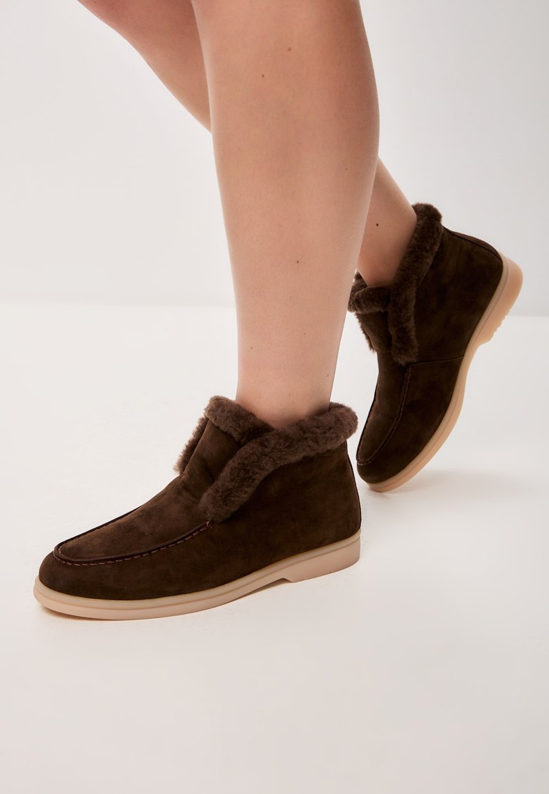 Bottines en daim marron avec un intérieur en fourrure douce, un bout rond et une semelle en caoutchouc clair avec des accents de couture.
