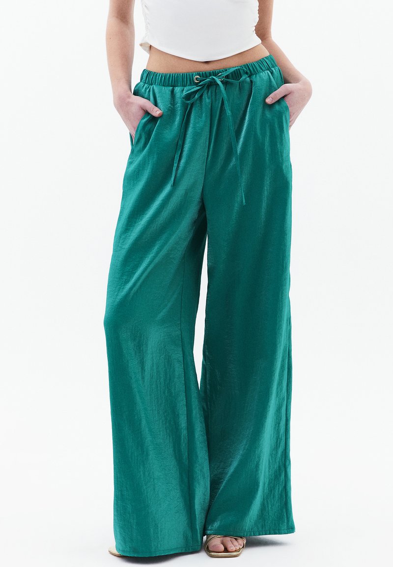 Wijdvallende broeken van glanzende teal stof met een elastische taille, trekkoordsluiting en zijzakken. Soepele textuur met een ontspannen pasvorm.