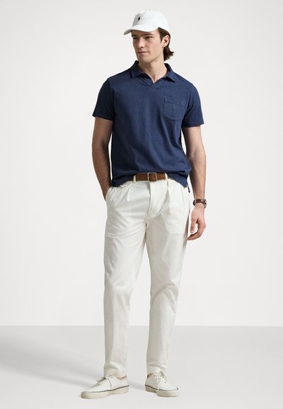 Polo bleu marine avec une poche, chinos blancs et baskets blanches. Casquette blanche avec des accents de logo. Style décontracté, coupe relax.