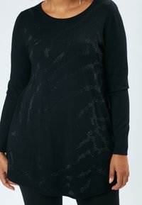 Schwarze Langarm-Tunika mit Rundhals, die ein strukturiertes Muster aus glänzenden Akzenten und gerippten Bündchen aufweist, entworfen für eine lockere Passform.