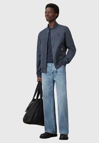 Námořnická bomber bunda, bavlna, se zipovým zapínáním, kombinována se světlomodrými širokými džínami. Nese černou tašku s logem na popruzích. Jednoduchý design.