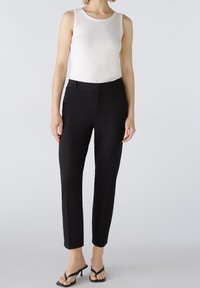 Pantalons noirs ajustés avec une coupe slim, dotés d'un devant plat et de poches latérales, associés à un débardeur blanc à côtes et des sandales noires.