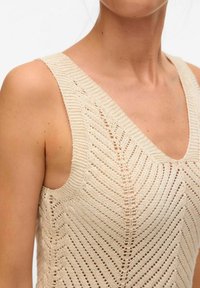 Heledad beež kootud tank top, millel on ševronmuster, sügav V-kaelus ja laiad rihmad tekstuurne viimistlus.