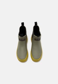 Bottes en caoutchouc vertes jusqu'à la cheville avec des semelles jaunes, présentant une languette noire et le logo Barbour à l'avant. Texture lisse et design épuré.