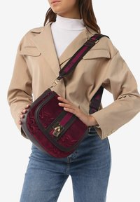 Borsa a tracolla color bordeaux realizzata in camoscio e pelle, con una chiusura dorata, una tracolla a righe e un motivo floreale in rilievo sul davanti.