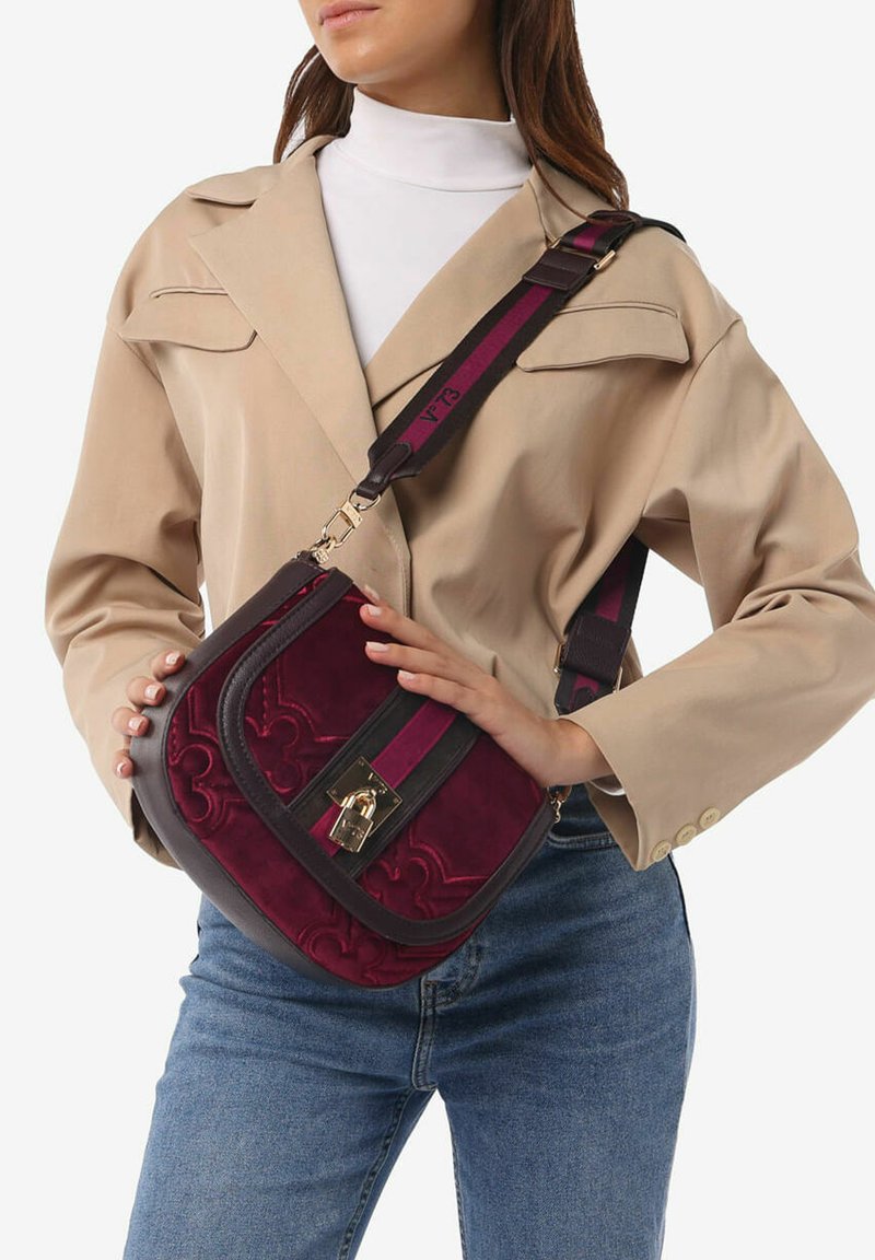 Borsa a tracolla color bordeaux realizzata in camoscio e pelle, con una chiusura dorata, una tracolla a righe e un motivo floreale in rilievo sul davanti.