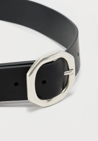 Fekete bőröv nagy, enyhén szabálytalan ezüstszínű fémből készült csattal, tekercsbe tekerve, fehér háttéren.