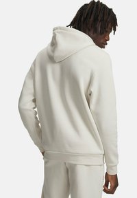 Hellbeiger Kapuzenpullover mit Kordelzugkapuze, weicher Textur und Kängurutasche. Das Modell ist von hinten zu sehen.