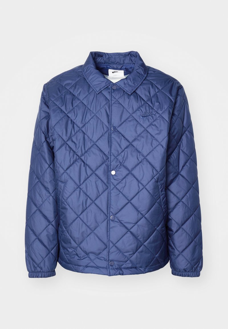 Veste matelassée bleu marine avec fermeture à bouton, manches longues et col. Fabriquée en matériau lisse et brillant avec un discret logo.