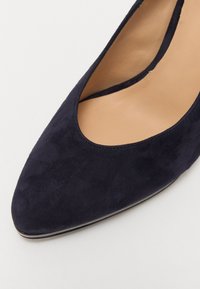 Chaussure à talon haut en daim bleu marine avec un bout pointu et un design découpé. Doublure intérieure lisse, silhouette élancée et bord de semelle brillant.