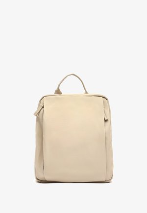 Mochila beige con una textura suave y mate, forma cuadrada, asa en la parte superior y detalle de cremallera visible en el lateral. Diseño simple sin patrones.