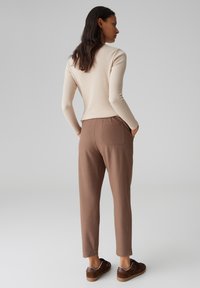 Maglietta a maniche lunghe beige chiaro a coste abbinata a pantaloni marroni a gamba affusolata con tasca posteriore, indossata con sneaker marroni con dettagli bianchi.