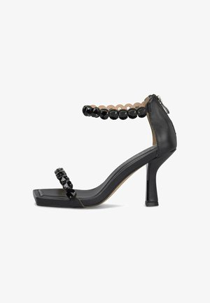 Sandalia negra de tacón alto con puntera cuadrada, tiras en el tobillo y en los dedos adornadas con cuentas negras facetadas, y cierre de cremallera trasero.