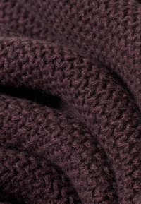 Dunkellila gestrickter Stoff mit einem strukturierten, erhabenen Muster. Weicher und dicker Stoff, der ein gemütliches, grobes Gewebe präsentiert.
