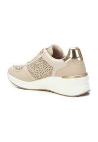 Zapatilla beige con detalles perforados, acentos dorados en el talón y una suela blanca. Diseñada con un material suave y una forma redondeada.