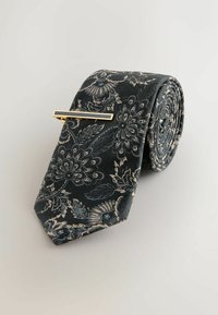 Donker bloemenpatroon stropdas van gestructureerde stof, gerold met een gouden stropdasclip met een rechthoekig ontwerp.