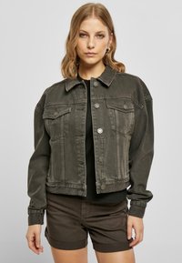 Dark gray denim jacket with a cropped design, button closure, two chest pockets, and long sleeves, worn over a black top and brown shorts.