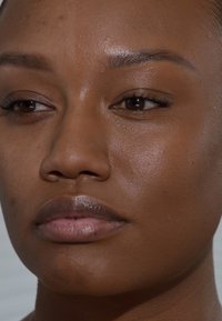 Close-up van een gezicht met een gladde, donkere huid. Kenmerken zijn volle lippen, gedefinieerde wenkbrauwen en bruine ogen met natuurlijke wimpers.