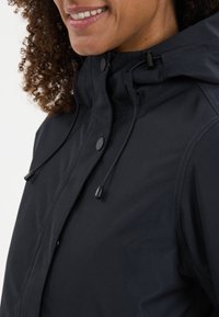 Giacca impermeabile nera con colletto alto, cappuccio regolabile e chiusure a pressione. Tessuto liscio con dettagli di cucitura discreti.