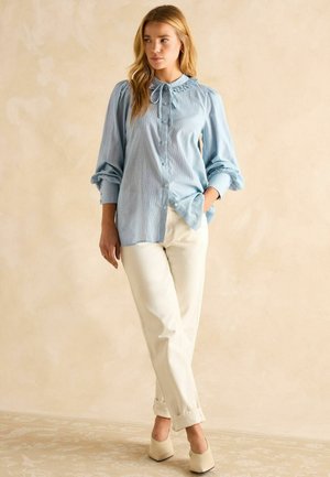 Hellblaues Button-Up-Bluse mit einem Rüschkragen und Puffärmeln, kombiniert mit weißen hochgerollten Hosen und nudefarbenen High Heels.