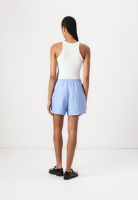 Shorts bleu clair avec des rayures verticales blanches, taille élastique et coupe décontractée. Associés à un débardeur blanc et des chaussures noires.