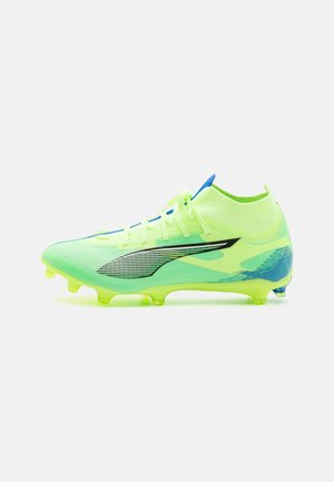 Botín de fútbol amarillo neón con un elegante upper de malla, acentos negros y lazos de cordones azules. Suela con tacos para tracción en superficies de hierba.