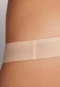 Ljusbeige midjeband med en slät, mjuk struktur, placerad mot en hudtonad bakgrund, med en platt söm i mitten.