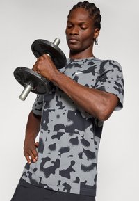 Hallide hallus hallitus shirt hallitus hallitus short sleeves ja ringkarbi, mis sisaldab erinevaid mustreid ja tekstuure, hoides hantlit.