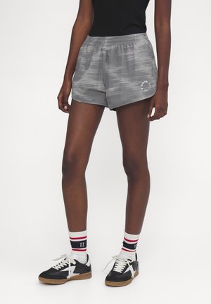 Graue Sportshorts mit strukturiertem Muster, elastischem Bund und weißen Grafiken, kombiniert mit schwarz-weißen Schuhen und gestreiften Socken.
