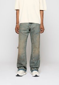 Ljusblå slitna jeans med en lös passform, som har rundade fickor, blekt utseende och uppkäftad nederdel, kombinerat med en krämfärgad topp och sneakers.