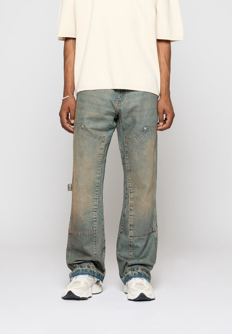 Ljusblå slitna jeans med en lös passform, som har rundade fickor, blekt utseende och uppkäftad nederdel, kombinerat med en krämfärgad topp och sneakers.