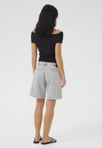 Melnas off-the-shoulder blūzes piegriezums kopā ar gaiši pelēkiem džinsu šortiem. Šorti ir brīvā piegriezuma ar redzamām aizmugures kabatām. Melnas flip-flops.