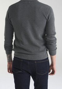 Maglione grigio a maglia con un motivo testurizzato, collo a giro, e maniche lunghe, abbinato a jeans scuri con tasche posteriori.
