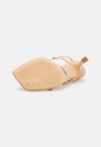 Soletta in gomma beige con motivo testurizzato, logo "GUESS" impresso, con un design a tacco sottile e cinturino.