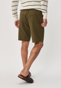 Olive green shorts with a drawstring waistband, featuring two back pockets and a smooth texture, paired with dark sandals and visible leg hair.