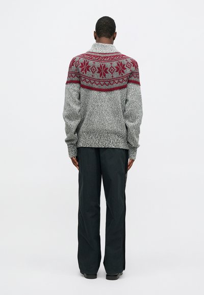 Grijze gebreide trui met een rode en gemusterde yoke, voorzien van een sjaalkraag. Gecombineerd met donker, wijder gesneden broeken.