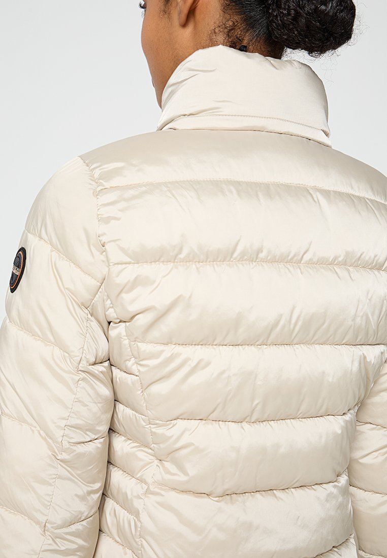Giacca puffer beige con colletto alto, cuciture orizzontali e texture lucida; presenta un logo circolare sulla spalla.