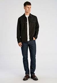 Zwart overhemd met knopen en twee borstzakken, gecombineerd met nauwsluitende donkerblauwe jeans en bruine veterschoenen. Eenvoudig ontwerp, gladde textuur.