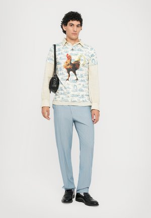 Long-sleeve shirt with rooster graphic in blue and cream tones, paired with light blue pinstripe trousers and black loafers.