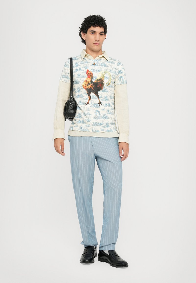 Langsleeve shirt met een afbeelding van een haan in blauwe en crèmekleurige tinten, gecombineerd met lichtblauwe gestreepte broek en zwarte instappers.