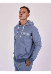 Blauwe hoodie van zacht materiaal, met een voorzak, witte trekkoorden en logo-opdruk op de borst. Geribbelde boorden en zoom.