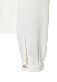 Witte lange mouwtop met gefronste manchetten met een gerimpelde rand, een kleine gouden knoop als accent en een zijsplit bij de pols.