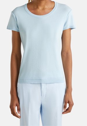 Personne portant un haut tricoté bleu clair à manches courtes avec des bords côtelés et un pantalon bleu clair assorti sur fond blanc.