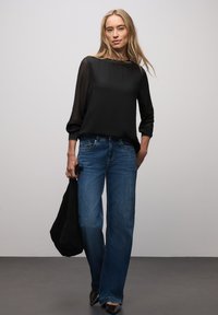 Blusa nera trasparente a maniche lunghe, jeans blu, borsa tote nera e scarpe nere con punta a punta. Outfit casual con vestibilità comoda e design minimalista.